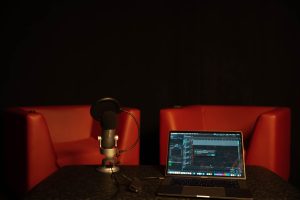 Zwei rote Sessel hinter Mikrofon und Notebook mit Podcastsoftware