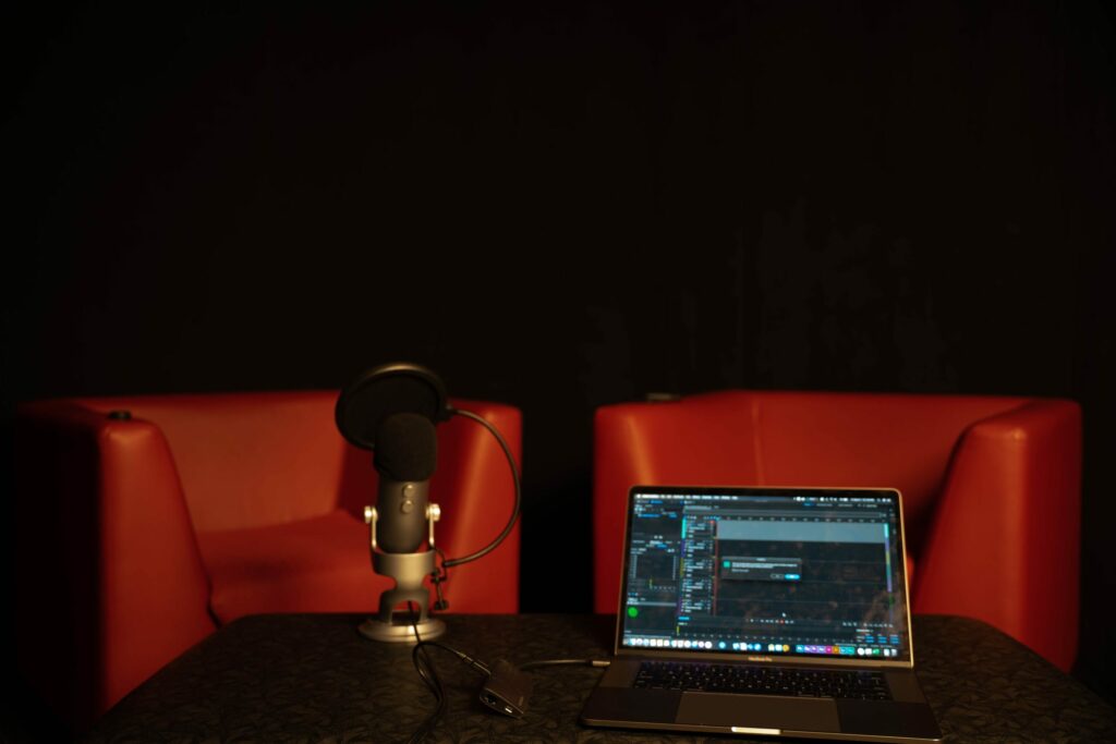 Zwei rote Sessel hinter Mikrofon und Notebook mit Podcastsoftware